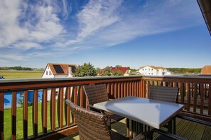 Un balcon avec une table et des chaises, donnant sur un quartier résidentiel avec des maisons et un ciel dégagé.
