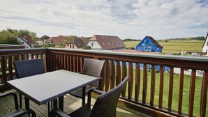 Un balcón con mesa y sillas, con vistas a una zona residencial con casas y un edificio azul.