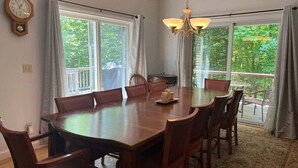 A dining room with a large wooden table, six chairs, a chandelier, and a view of greenery outside. - Pet Friendly Private Home, Located in Forest Ridge (Lincoln)