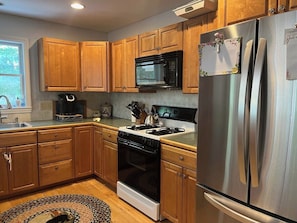 Una cocina con armarios de madera, un refrigerador de acero inoxidable, microondas, estufa y cafetera.