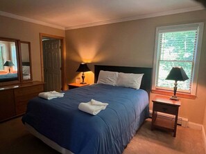 Un lit bien fait, avec une literie bleue, une lampe de chevet, une table de nuit en bois et un miroir accroché au mur.