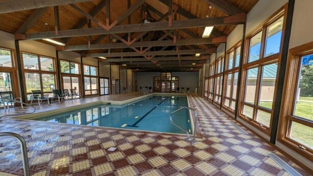 An indoor swimming pool with a tiled floor, wooden beams, and large windows. - Pet Friendly Private Home, Located in Forest Ridge (Lincoln)