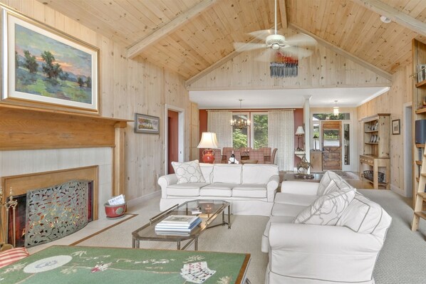 A spacious living room with a high ceiling, wooden walls, a fireplace, a sofa set, a coffee table, and a dining area with a table and chairs. - Marvelous Home in the Highly Desired Highlands Falls Country Club Community | Falls Drive Cottage (Highlands)
