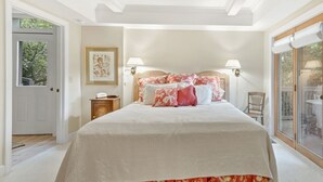 Ein Schlafzimmer mit einem großen Bett, zwei Nachttischlampen, einem gerahmten Bild an der Wand und Blick durch eine Glastür.