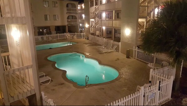 Relax by the oval-shaped pool surrounded by lounge chairs and a modern building with balconies.