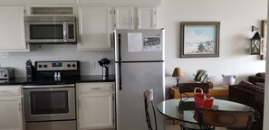 Compact kitchen with stainless steel appliances, microwave, oven, and refrigerator. Dining area with a glass table and single chair.