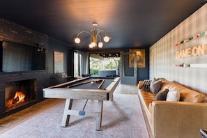 Une table de billard dans une pièce avec une cheminée, un canapé et un panneau lumineux au néon.