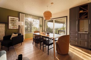 Une cuisine moderne avec des meubles de couleur sombre, un coin repas avec une table et des chaises en bois, un canapé noir et une grande fenêtre offrant une belle vue.