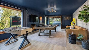 Ein modernes Wohnzimmer mit Tischfußball, Billardtisch und Kamin.