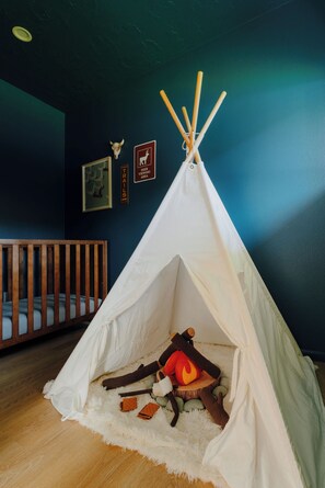 A white teepee with a fire inside, set up in a room with a wooden crib and wall decorations. - Epic Game Room, Outdoor Movie Night, Hot Tub, Fire Pit (The Dalles)