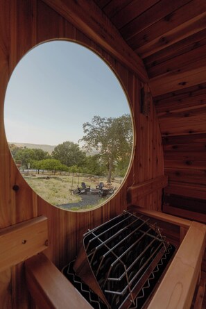 A circular window with a view of a grassy area, trees, and a distant hill. - Epic Game Room, Outdoor Movie Night, Hot Tub, Fire Pit (The Dalles)