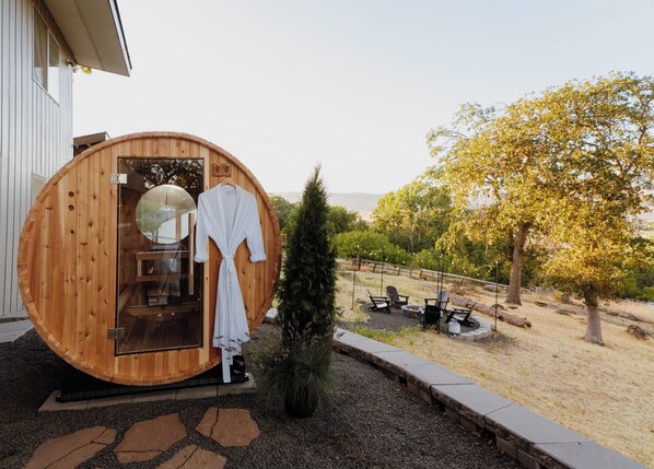 Une structure de sauna en bois, dotée d’une porte, d’un petit arbre et de sièges extérieurs.