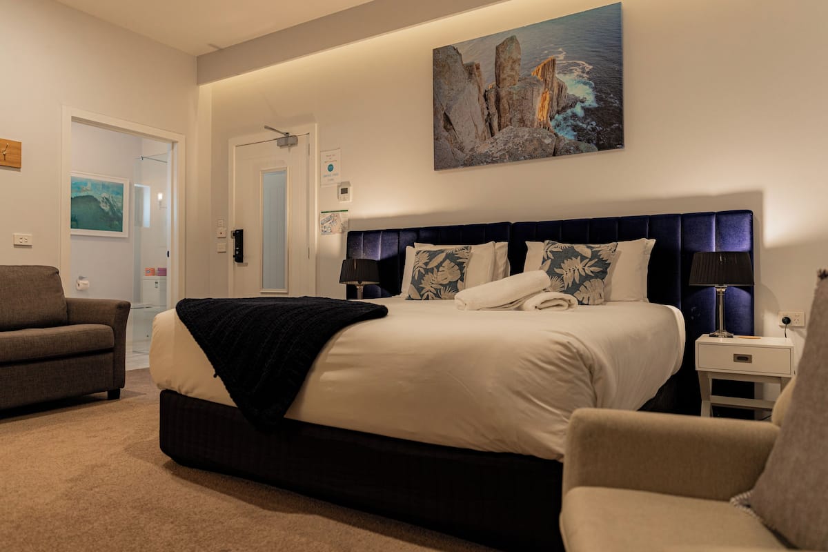 A modern bedroom with a large bed, a sofa, and a painting on the wall.