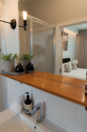 A modern bathroom with a wooden vanity, a mirror, and two potted plants. - Bay Of Fires Apartments (St Helens)