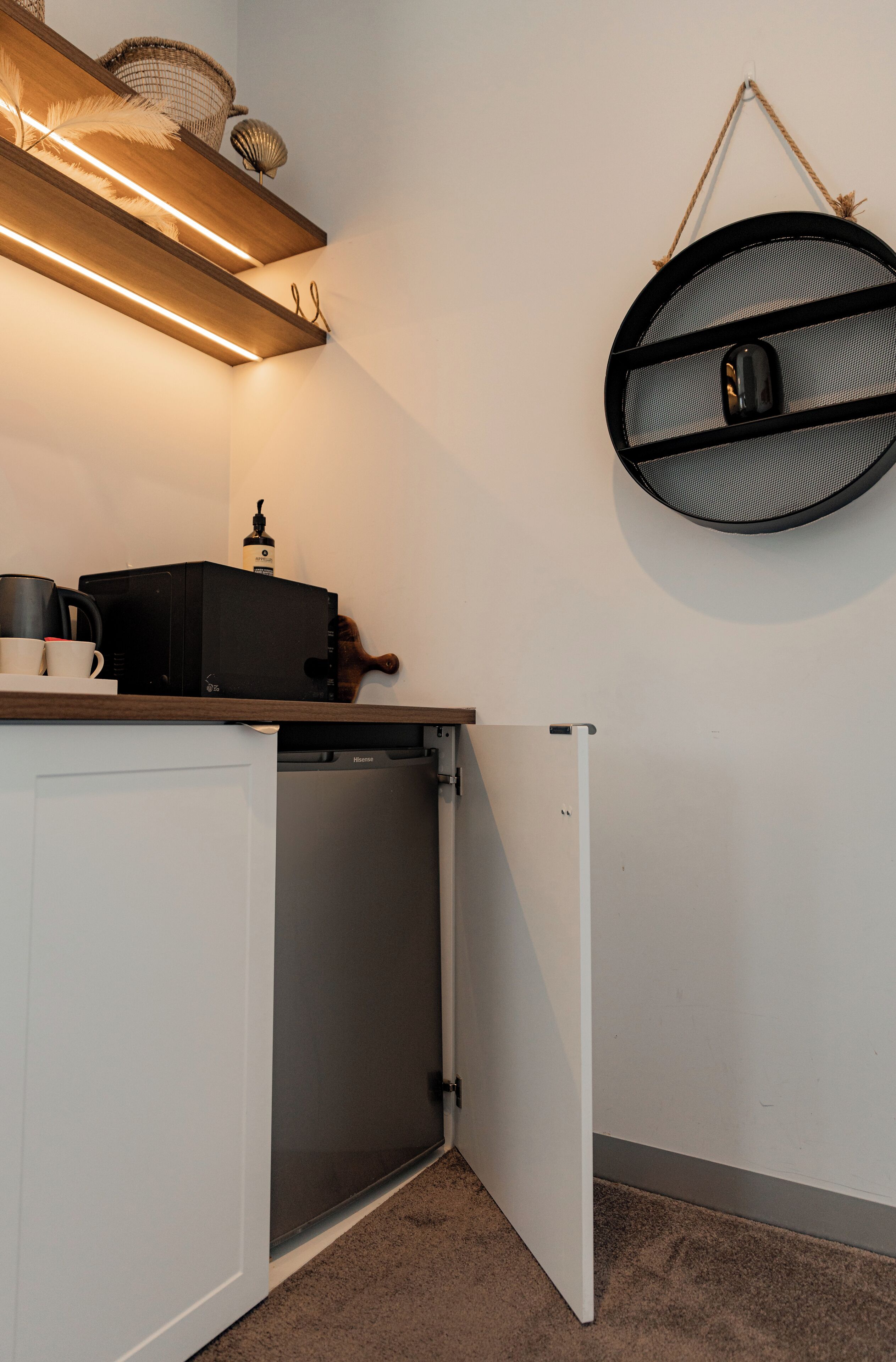 Une cuisine compacte équipée d’un lave-vaisselle encastré, d’une machine à café et d’un haut-parleur suspendu.