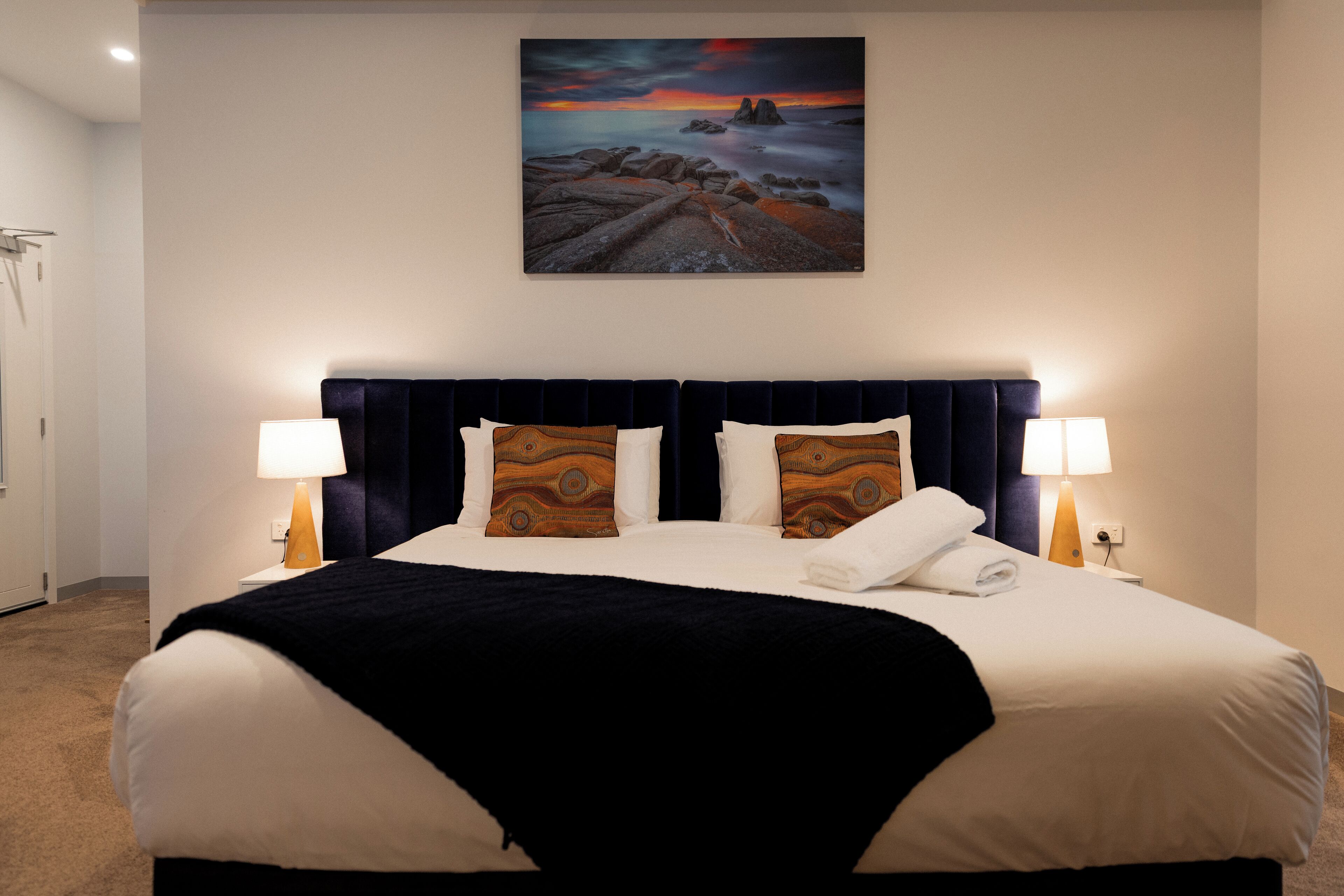 Habitación de hotel con una cama grande, dos lámparas de noche, un cuadro en la pared y vistas al exterior.