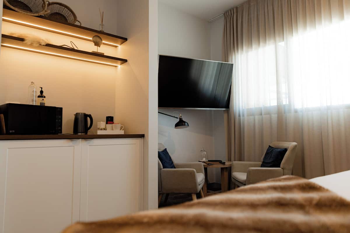 A modern hotel room with a flat-screen TV, two chairs, a small table, and a minibar.