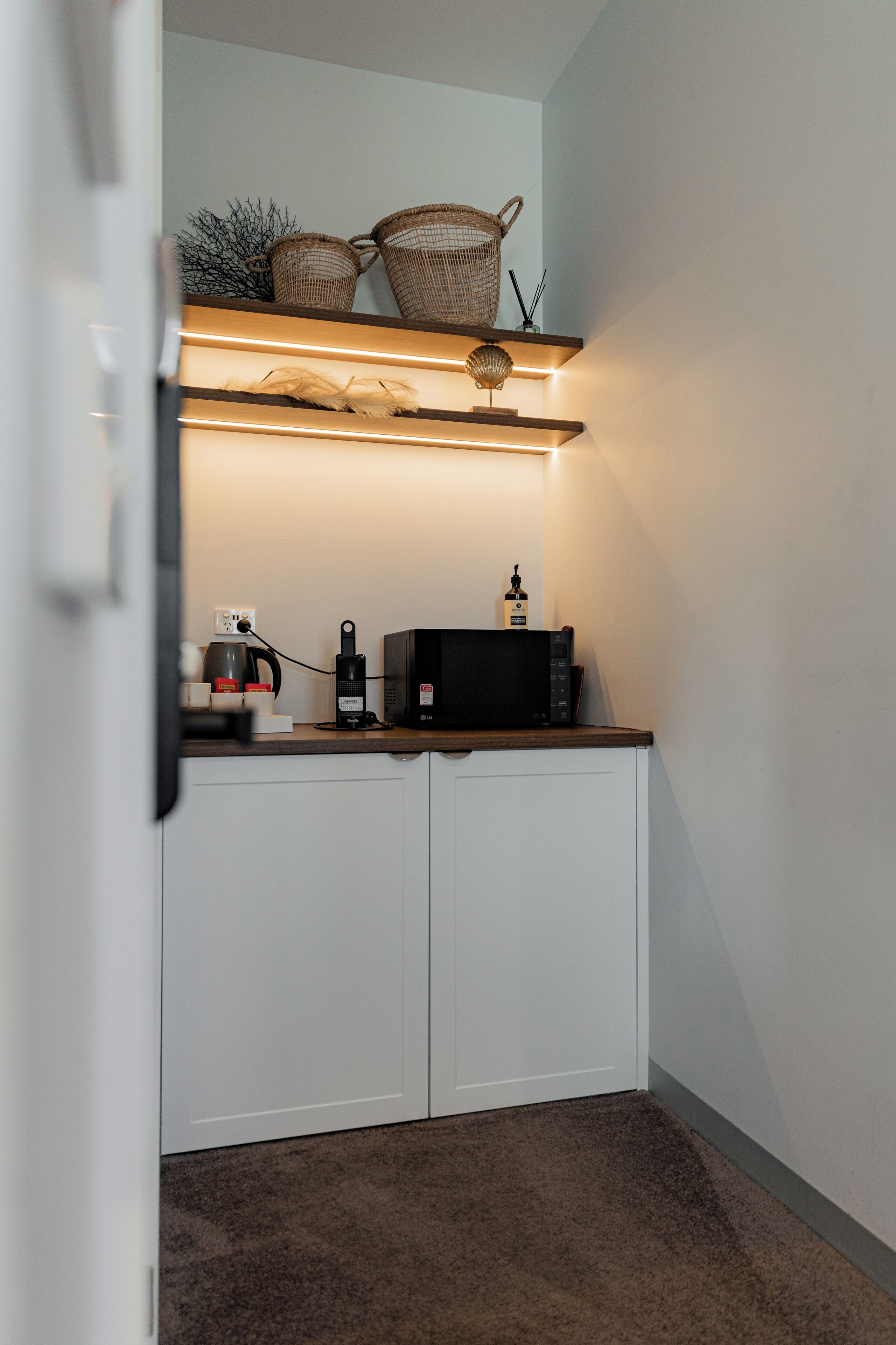 A kitchenette with a coffee maker, microwave, and a small shelf with baskets.