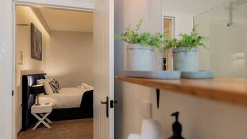 Una habitación de hotel con cama, mesita de noche, lámpara y una planta en un estante.