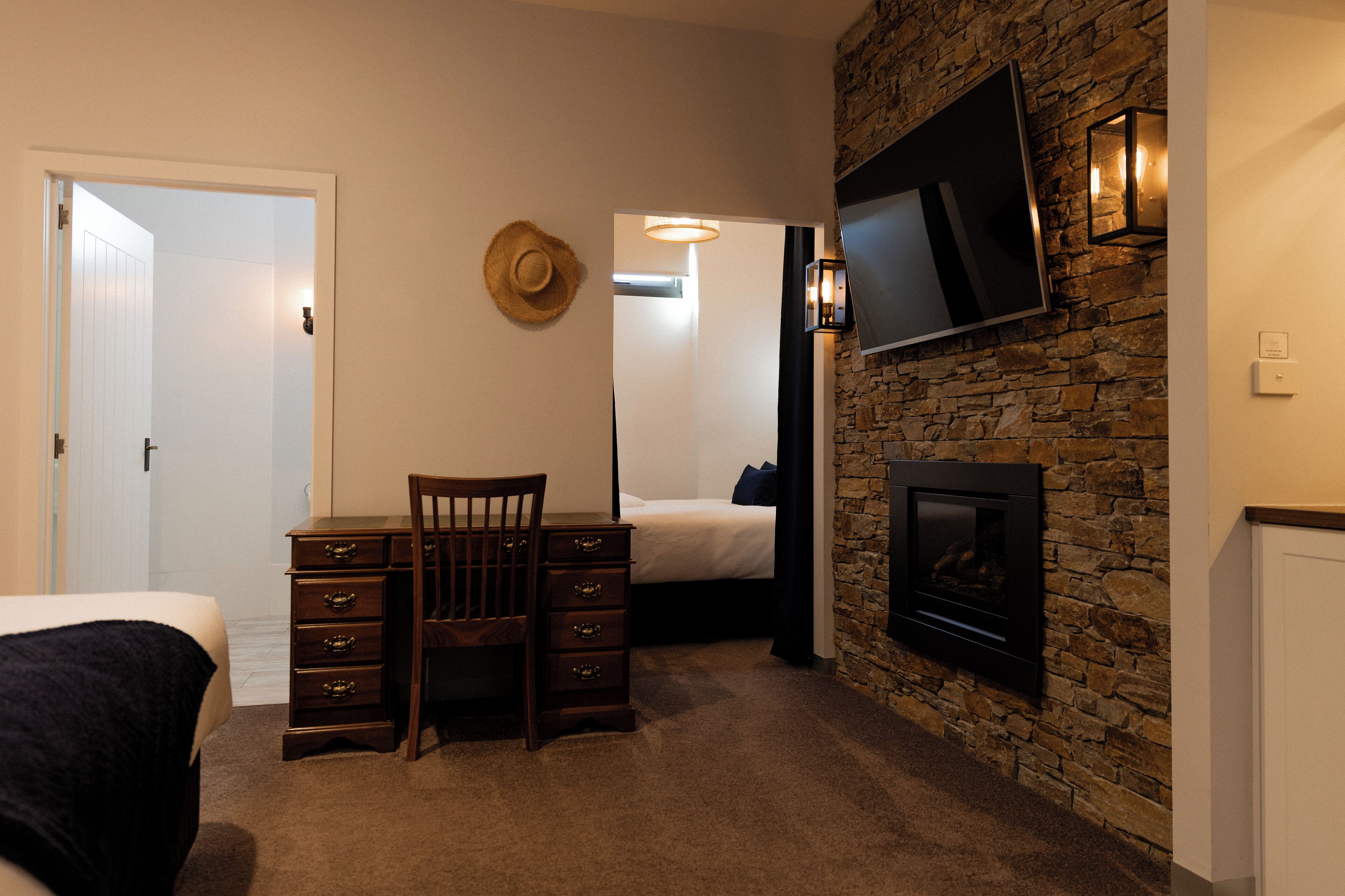 Une chambre à coucher comprenant un lit, une commode, une chaise, un téléviseur fixé au mur en pierre et une cheminée.