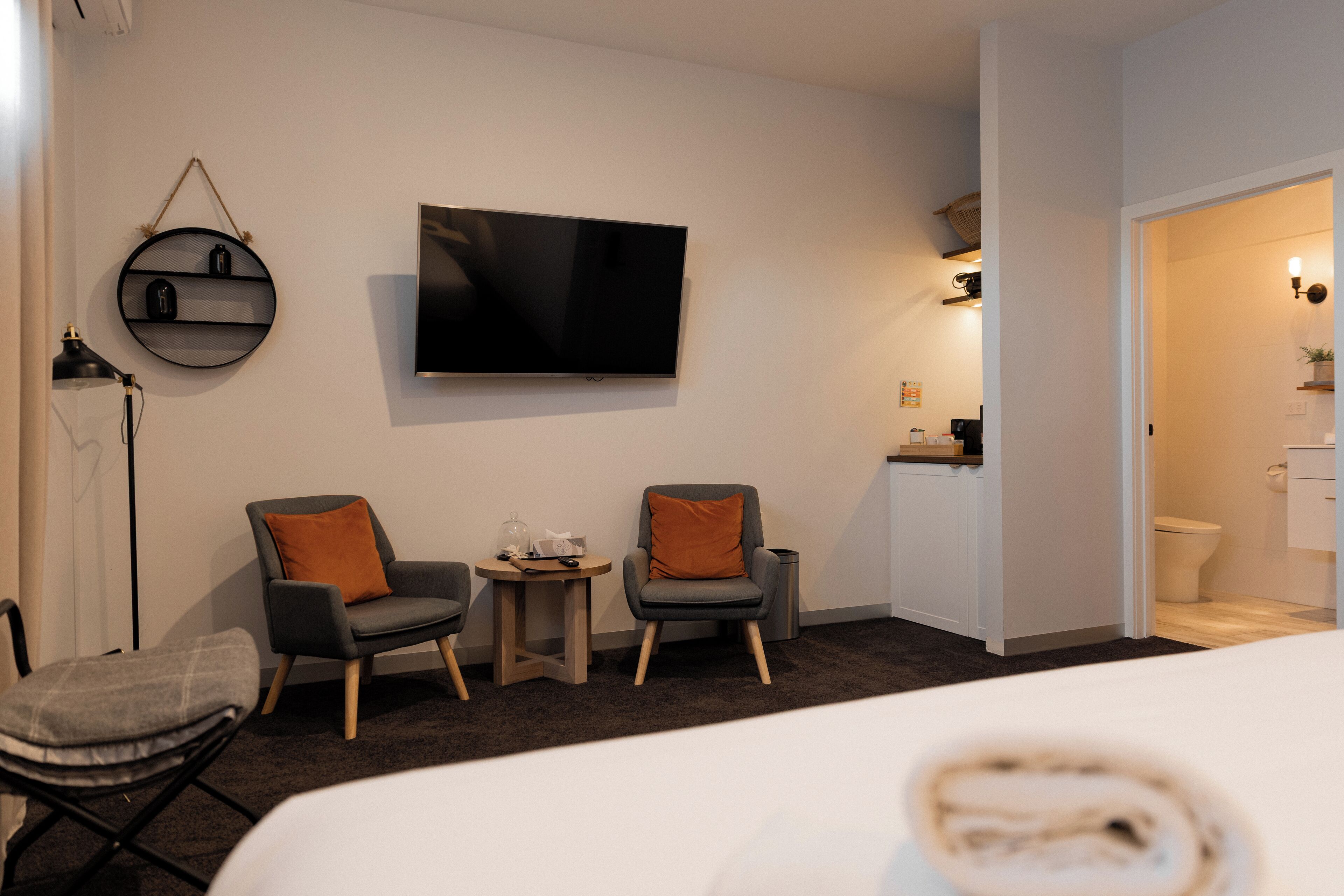 Ein Hotelzimmer mit einem Bett, zwei Sesseln, einem kleinen Tisch, einem Fernseher und einem durch eine offene Tür einsehbaren Badezimmer.