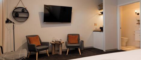 Ein Hotelzimmer mit einem Bett, zwei Sesseln, einem kleinen Tisch, einem Fernseher und einem durch eine offene Tür einsehbaren Badezimmer.