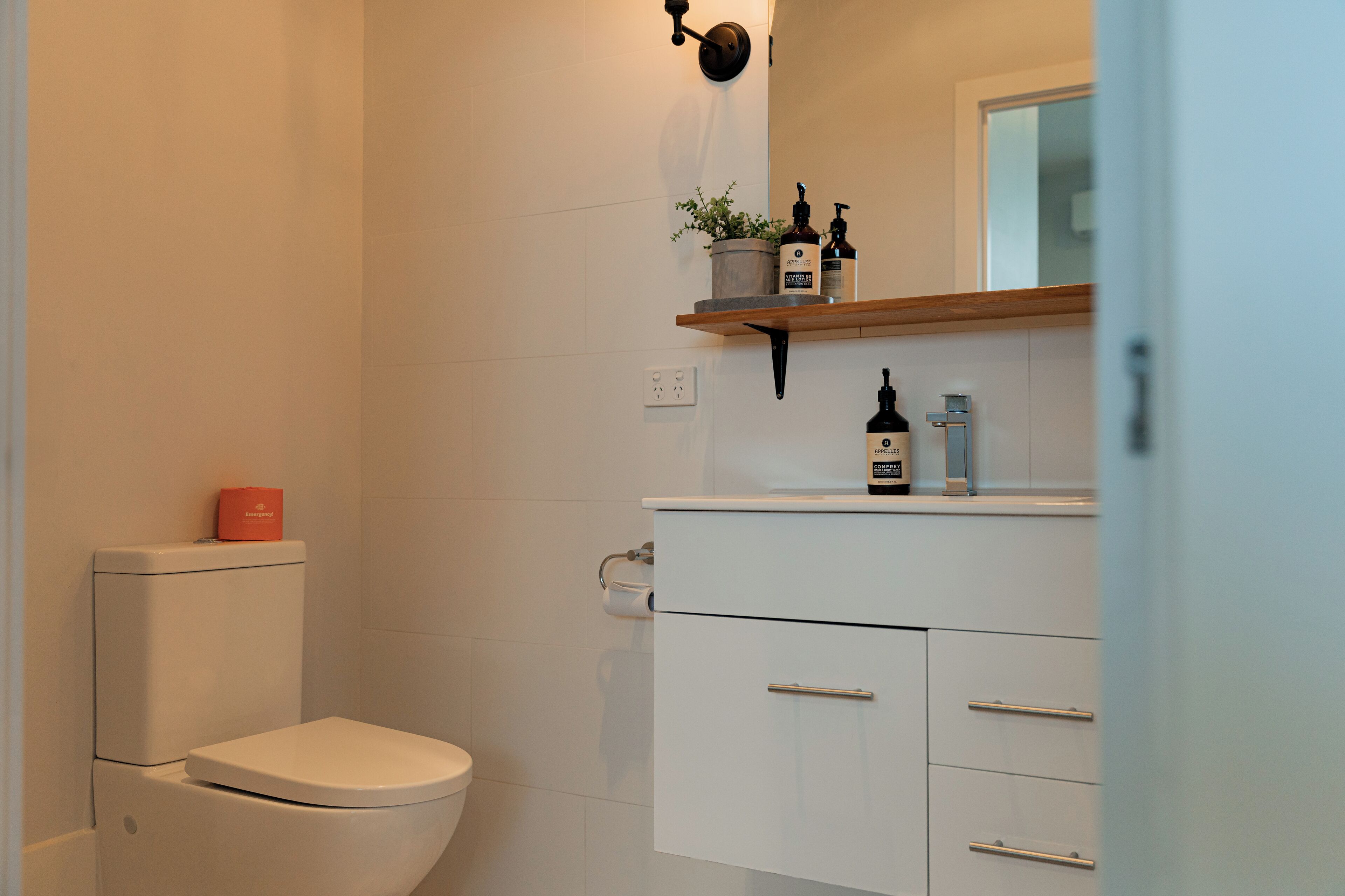Un baño moderno con inodoro, lavamanos y estante con artículos de aseo.