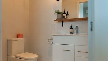 Un baño moderno con inodoro, lavamanos y estante con artículos de aseo.