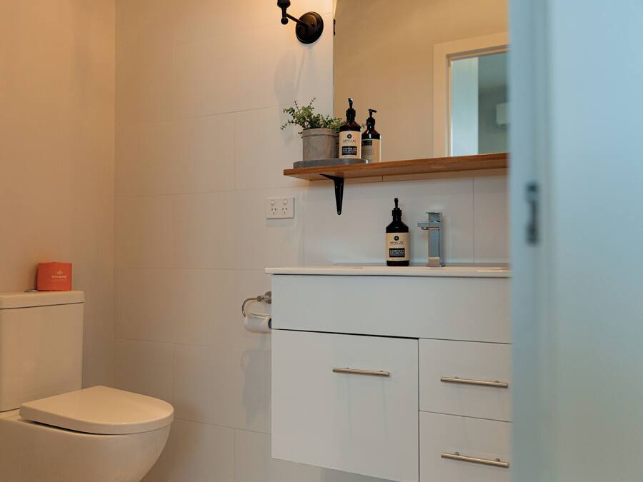 Un baño moderno con inodoro, lavamanos y estante con artículos de aseo.