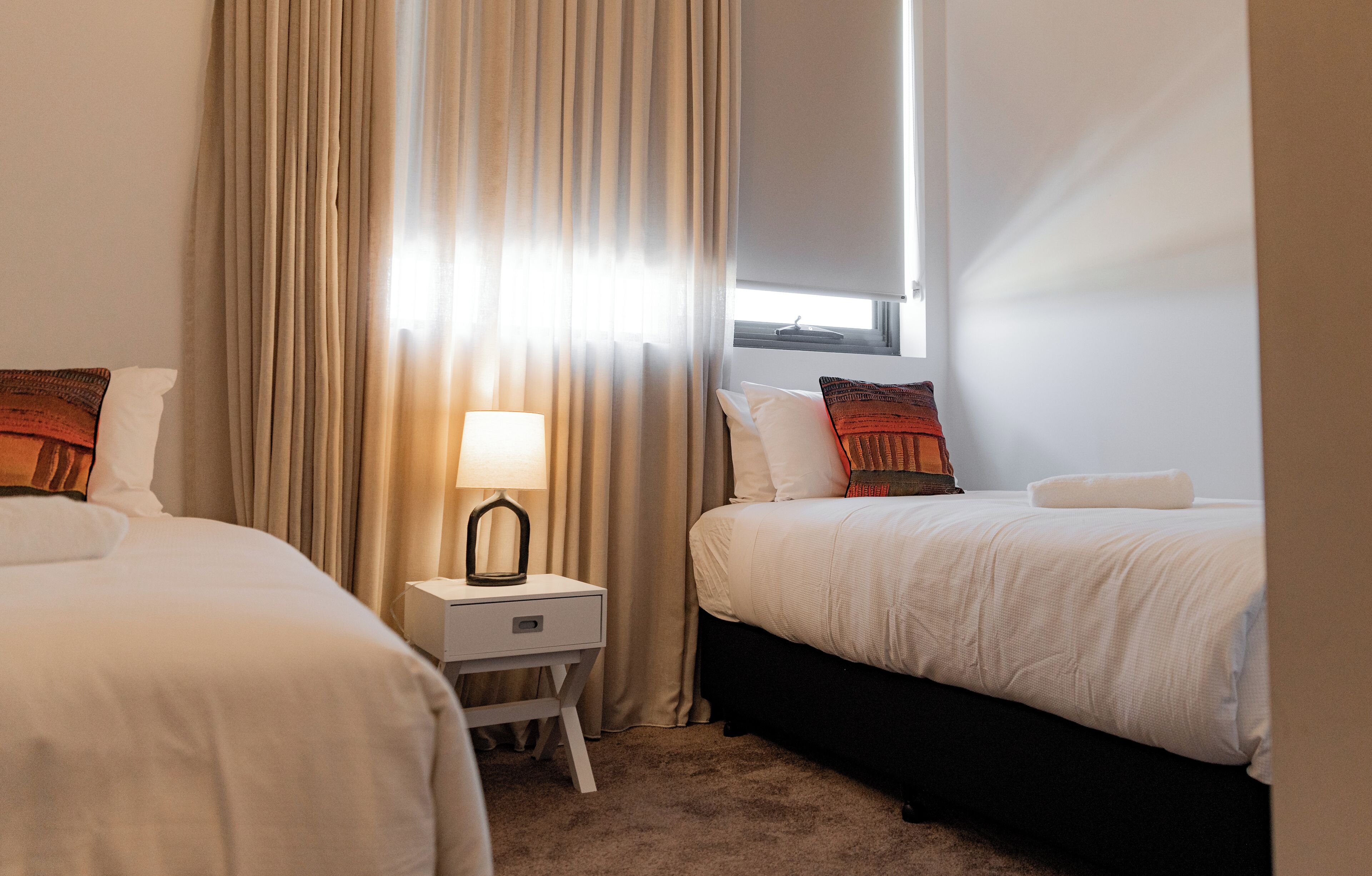 Une chambre d’hôtel avec deux lits, une table de chevet avec une lampe et une fenêtre avec des rideaux.