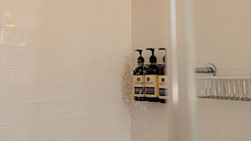 A shower with a square head, a handheld showerhead, and a wall-mounted control panel with bottles of toiletries.