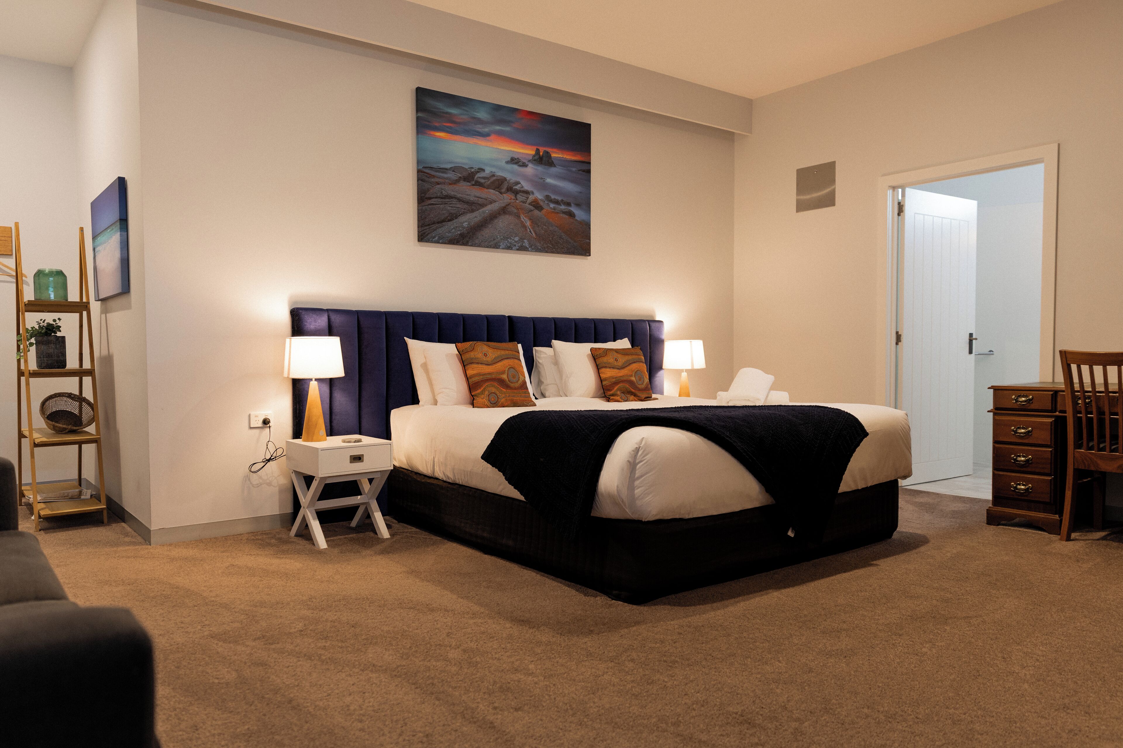 A bedroom with a large bed, two bedside tables, a nightstand, a chair, and a door.