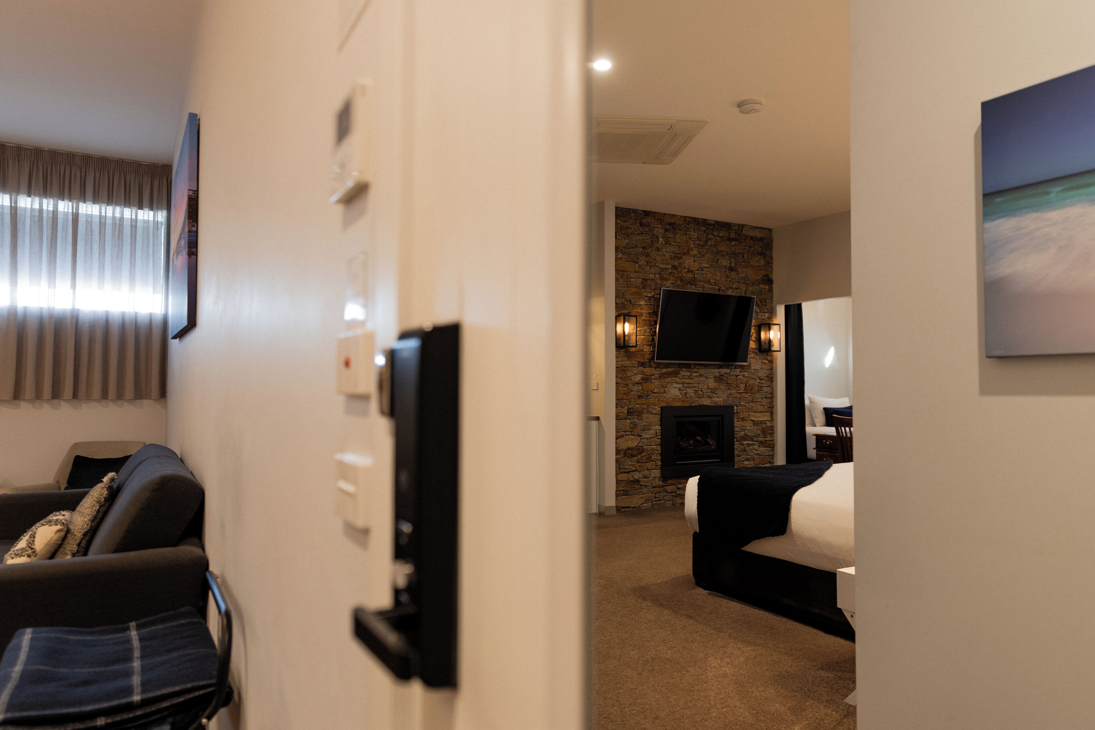 A hotel room with a stone fireplace, a flat-screen TV mounted on the wall, and a bed with a white comforter.