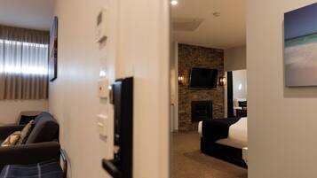 A hotel room with a stone fireplace, a flat-screen TV mounted on the wall, and a bed with a white comforter.