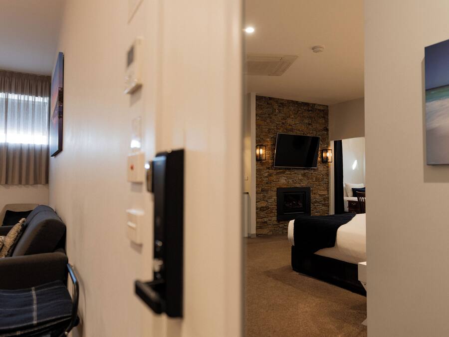Habitación de hotel con chimenea de piedra, televisor de pantalla plana montado en la pared y cama con cubrecama blanco.