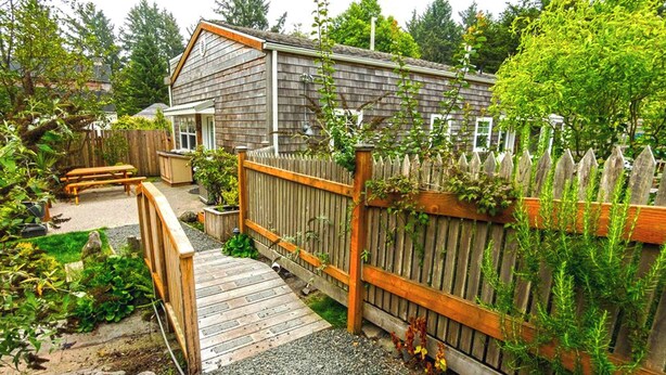 Een houten terras dat leidt naar een huis met een omheinde achtertuin, een bankje en een tuin.