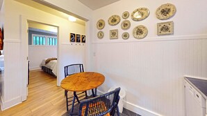 Een eetruimte met een ronde houten tafel en stoelen, een gang naar een slaapkamer, en een wand versierd met borden.