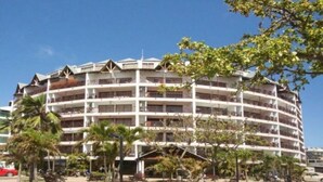 Un hotel de varios pisos con balcones, rodeado de palmeras y bancos.