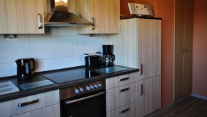 Een compacte keuken met houten kastjes, een roestvrijstalen afzuigkap, een koffiezetapparaat en een magnetron.
