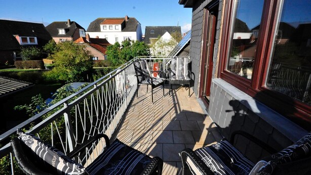 Een balkon met tuinmeubilair, uitzicht op omliggende huizen en een heldere lucht.