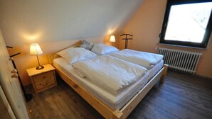 Een slaapkamer met een houten bed, twee nachtkastjes met lampen, een radiator en een raam met uitzicht.