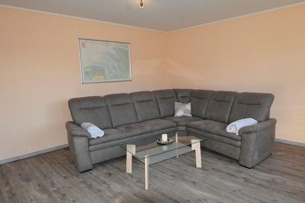 A living room with a grey sectional sofa, a glass coffee table, and a map on the wall.