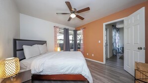 A bedroom with a bed, a ceiling fan, a nightstand, and a door leading to another room. - Condo in the heart of the Catalina Foothills (Tucson)