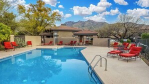 A swimming pool with red lounge chairs and a building with a tiled roof in the background. - Condo in the heart of the Catalina Foothills (Tucson)