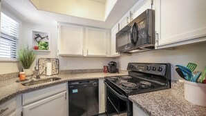 A modern kitchen with white cabinets, a stainless steel microwave, a black stove, and a dishwasher. - Condo in the heart of the Catalina Foothills (Tucson)