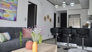 Ein modernes Wohnzimmer mit einer Couch, einem Couchtisch mit Vasen und einer Küche im Hintergrund.