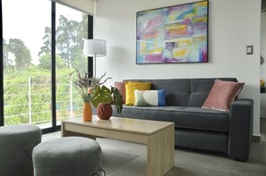 A modern living room with a grey sofa, colorful cushions, a wooden coffee table, and a large abstract painting on the wall.