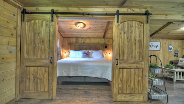 A wooden room with a bed, a wall-mounted light fixture, and a sign that reads "house". - The Barn with a  Hot Tub, Fire Pit and Pet Friendly (Blue Ridge)