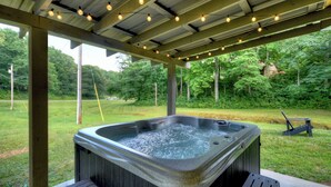 A hot tub under a wooden pergola with string lights, surrounded by a grassy area and trees. - The Barn with a  Hot Tub, Fire Pit and Pet Friendly (Blue Ridge)