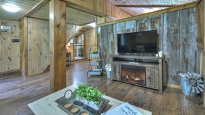 A rustic interior with wooden walls, a fireplace, a television, and a dining area with a table and chairs. - The Barn with a  Hot Tub, Fire Pit and Pet Friendly (Blue Ridge)